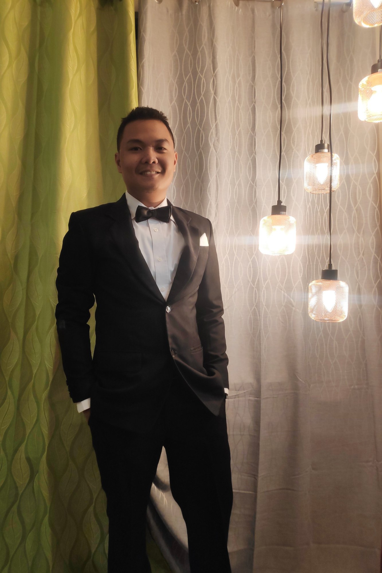 Reymar, professional WordPress designer, wearing a black tuxedo and bow tie, standing indoors with decorative lighting.