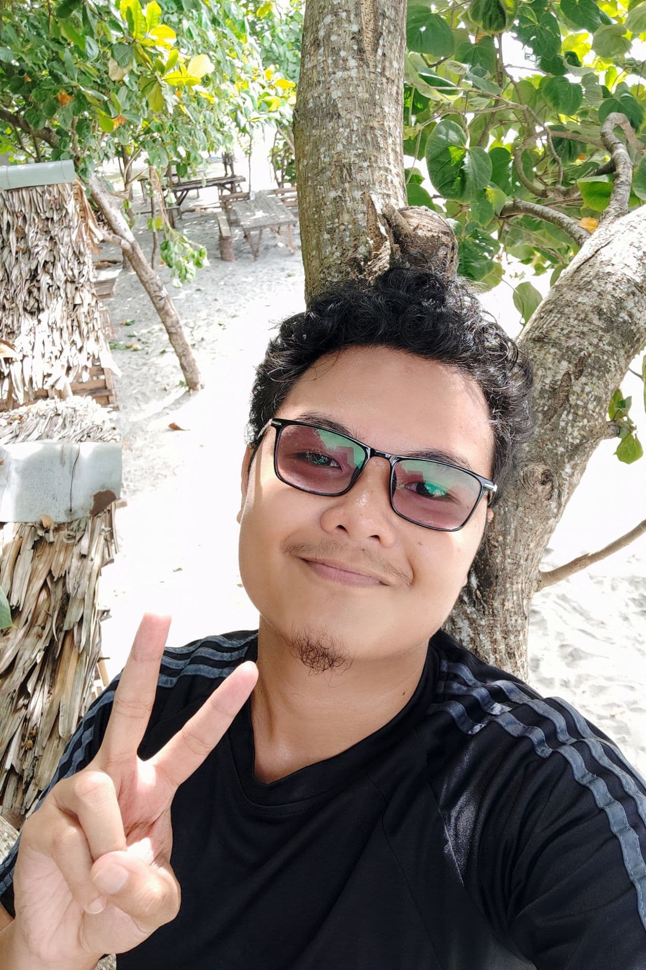 Reymar, WordPress designer, smiling and making a peace sign at the beach under a tree.
